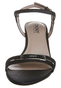 Czarne sandały na obcasie DKNY z gładkim wyściółkiem, smukłym paskiem wokół kostki oraz detalami w srebrnym odcieniu na górnej części.