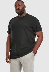 T-shirt nera a maniche corte con collo rotondo e vestibilità morbida, abbinata a pantaloni tuta grigi per un look casual.