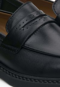 Black leather loafers with a smooth finish, featuring a wide strap across the top and small perforations, set on a textured rubber sole.