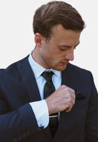 Traje navy con corbata de paisley negro; camisa blanca con puños en contraste; hombre ajustando un pañuelo negro en el bolsillo, diseño minimalista, corte entallado.