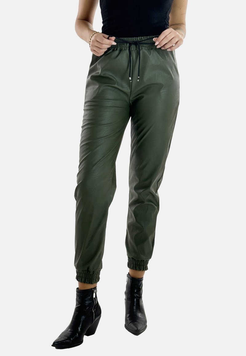 Olivgrüne Jogginghosen aus glattem, glänzendem Material, mit einem elastischen Bund und Knöchelbündchen. Kombiniert mit schwarzen Absatzstiefeln.