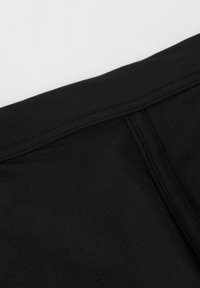 Svart bomullsduk med en mjuk textur, som har en midjeband och sömmar, sedd från en närbild. Inga mönster eller detaljer närvarande.