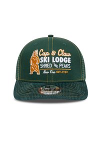 Gorra verde con un diseño estructurado, que presenta texto bordado y un gráfico de un oso. Tiene un cierre tipo snapback y un visera plana. El texto es de color naranja y blanco.