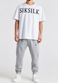 Hvid bomulds t-shirt med "SIKSILK" logo i sort; parret med grå sweatpants med sidelommer og elastiske manchetter, iført med hvide sneakers.
