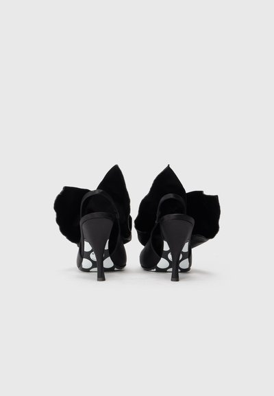 Sapatos pretos de salto alto feitos de veludo, apresentando um design afiado na parte de trás e um padrão ousado de bolinhas brancas nas solas.