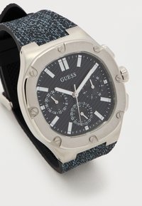 Ρολόι Guess με ασημένιο εξαγωνικό πλαίσιο, μαύρο υφασμάτινο καντράν με υφή, πολυλειτουργικά υποκαντράν, φωσφορίζοντες δείκτες και μπλε-μαύρο υφασμάτινο λουρί.