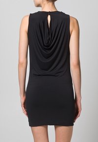 Czarna sukienka bez rękawów z drapowaną tylną częścią, wycięciem w kształcie łezki przy szyi oraz gładkim, elastycznym materiałem, dopasowana w górnej części uda.