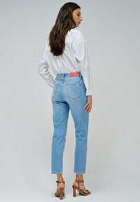 Vaqueros de tiro alto azul claro con pierna recta, bolsillos traseros de parche y un parche de logo de cuero rojo visible en la cinturilla.