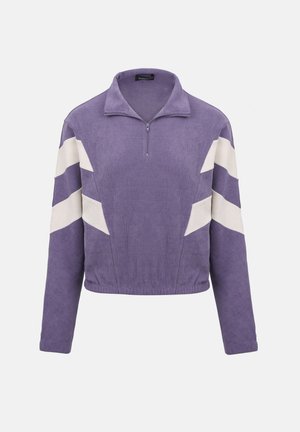 Lilla genser med lange ermer, hvite sikksakkstriper på ermene, kvartglidelås i kragen, og elastisk midjebånd på ensfarget bakgrunn.