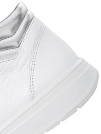 Close-up of white leather sneaker heel with metallic silver padded collar and textured white rubber sole.