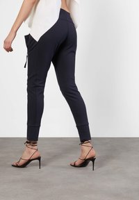 Dunkelblaue, enganliegende Hose mit elastischem Bund, schmal zulaufenden Beinen und seitlichen Taschen, kombiniert mit schwarzen, schmalen High-Heels mit Riemchen.