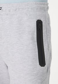 Gray athletic jogger pants in soft fabric with a black zippered pocket on the side, featuring a textured waistband.