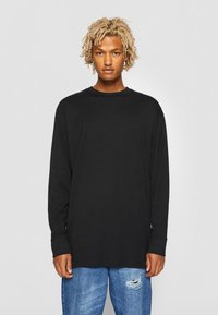 T-shirt noir à manches longues en coton doux, avec col rond et coupe ample, associé à un jean bleu clair déchiré.