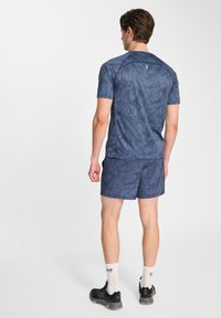 Mörkblå idrottströja med ett texturerat mönster, ihop med matchande shorts. Materialet verkar lätt och andas. Svarta sneakers ingår.