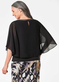 Schwarzes Oberteil mit fließenden Ärmeln, featuring eine Schlüsselloch-Rückseite und einen strukturierten Kragenband. Kombiniert mit einem gemusterten Rock in gedämpften Farben.