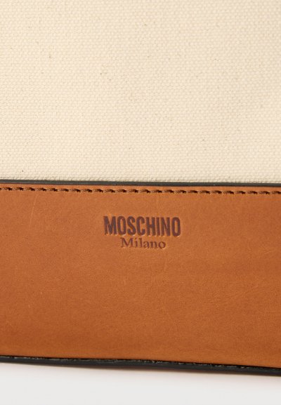 Μπεζ ύφασμα και καφέ δέρμα με ραμμένη άκρη, με το όνομα της μάρκας "Moschino Milano" χαραγμένο στο δερμάτινο τμήμα.
