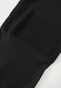 Vêtement noir avec une partie inférieure lisse et extensible et une partie supérieure texturée et douce. Présente une couture en tissu contrastant.