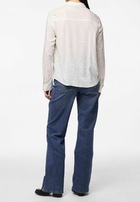 Light, long-sleeved blouse with a white base, small colorful floral patterns, and a curved hem, paired with dark blue, wide-leg jeans.