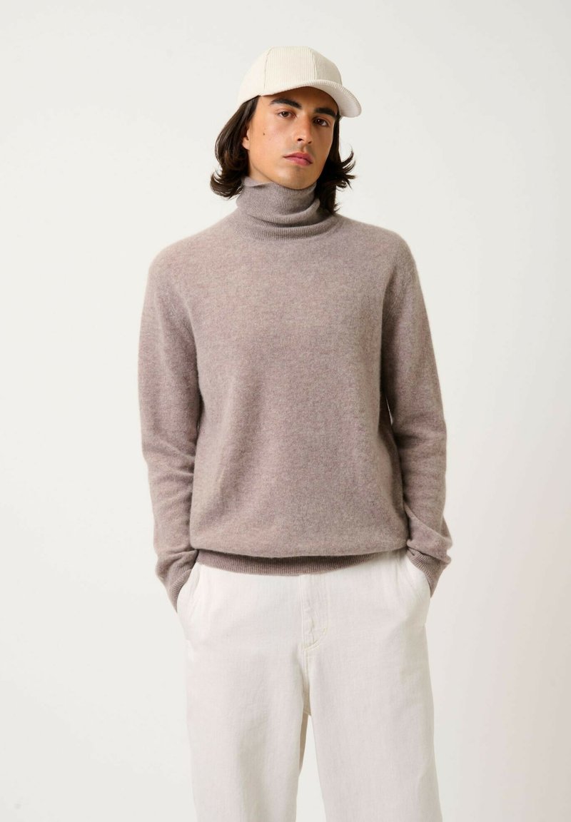 Maglione grigio chiaro a collo alto realizzato in morbida lana, con maniche lunghe e orlo a coste. Abbinato a pantaloni bianchi larghi e un cappello beige.