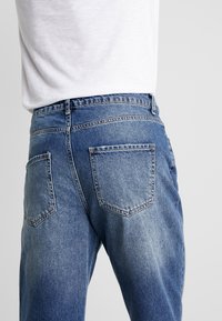 Denim jeans in light blue, featuring a regular fit, five-pocket design, and a slightly faded texture. Waistband with belt loops visible.