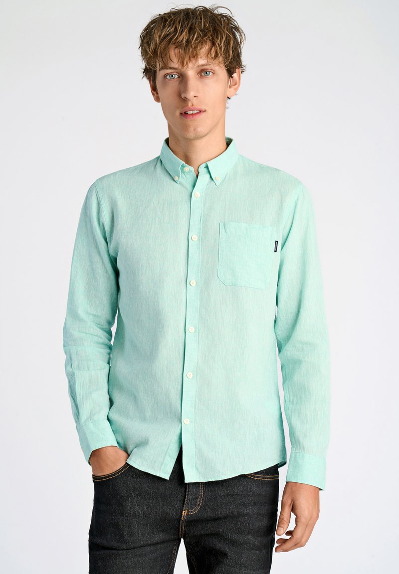 Miętowa koszula na guziki z kieszonką, długimi rękawami i luźnym krojem. Szczegóły tkaniny teksturowanej, noszona z ciemnymi dżinsami.