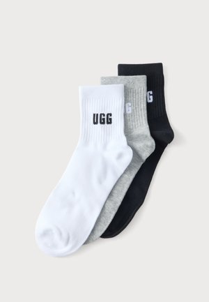 Τρία ζευγάρια κάλτσες UGG σε λευκό, γκρι και μαύρο, στοιβαγμένα και απλωμένα επίπεδα σε ένα απλό ανοιχτό φόντο.
