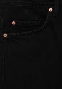 Tissu en denim noir en gros plan montrant une poche avant avec des rivets en cuivre et des coutures détaillées.