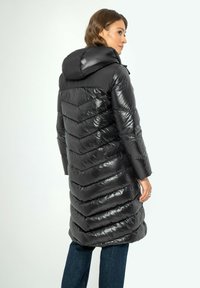 Schwarze Daunenjacke mit einem Chevron-steppdesign, ausgestattet mit einer Kapuze, glänzender Textur und langen Ärmeln, kombiniert mit blauen Jeans.