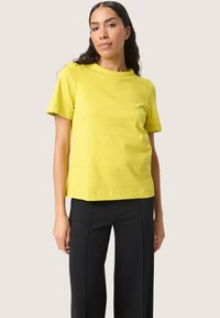 Yellow cotton t-shirt with short sleeves, round neckline, and a relaxed fit, paired with black straight-leg trousers.
