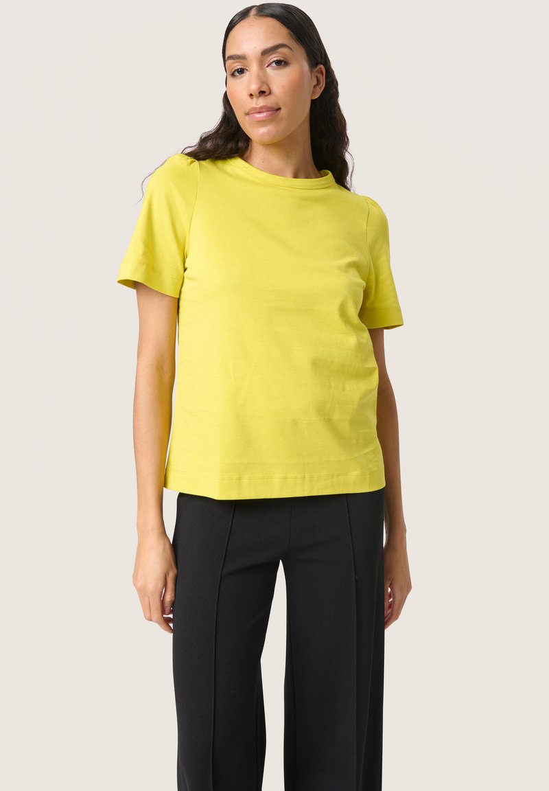 Yellow cotton t-shirt with short sleeves, round neckline, and a relaxed fit, paired with black straight-leg trousers.