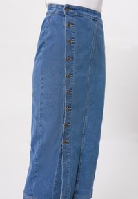 Jeanskjol i en blå nyans med sidoknappar som har bruna knappar, samt en kontrasterande texturpanel.