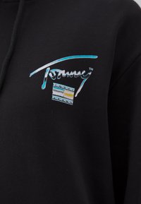 Sudadera negra con un logo frontal que presenta texto en turquesa y blanco, acompañado de un gráfico rectangular en azul, gris, amarillo y blanco.
