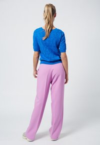 Suéter de punto texturizado azul con mangas cortas, combinado con pantalones rosa de talle alto y corte holgado. El calzado son zapatillas de colores claros.