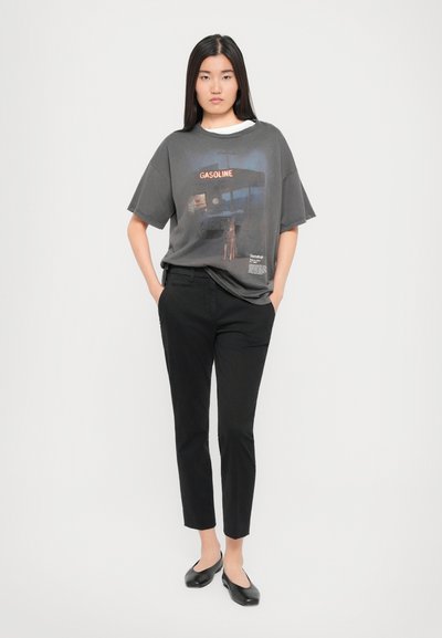 T-shirt graphique gris avec un imprimé de station-service, associé à un pantalon noir slim et des ballerines noires. Design simple et décontracté.