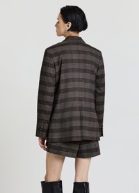 Brauner karierter Blazer mit strukturierter Schnittführung, versehen mit grauen und weißen Streifen. Kombiniert mit passenden Shorts, die eine maßgeschneiderte Passform zeigen.