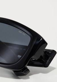 Sorte sports solbriller med mørke linser, der har en robust ramme og et unikt hængselsdesign. Graveret "Nike Max" på linsen.