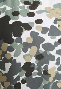Tejido con un patrón que presenta formas abstractas en verde, negro y beige sobre un fondo blanco, con una textura suave.