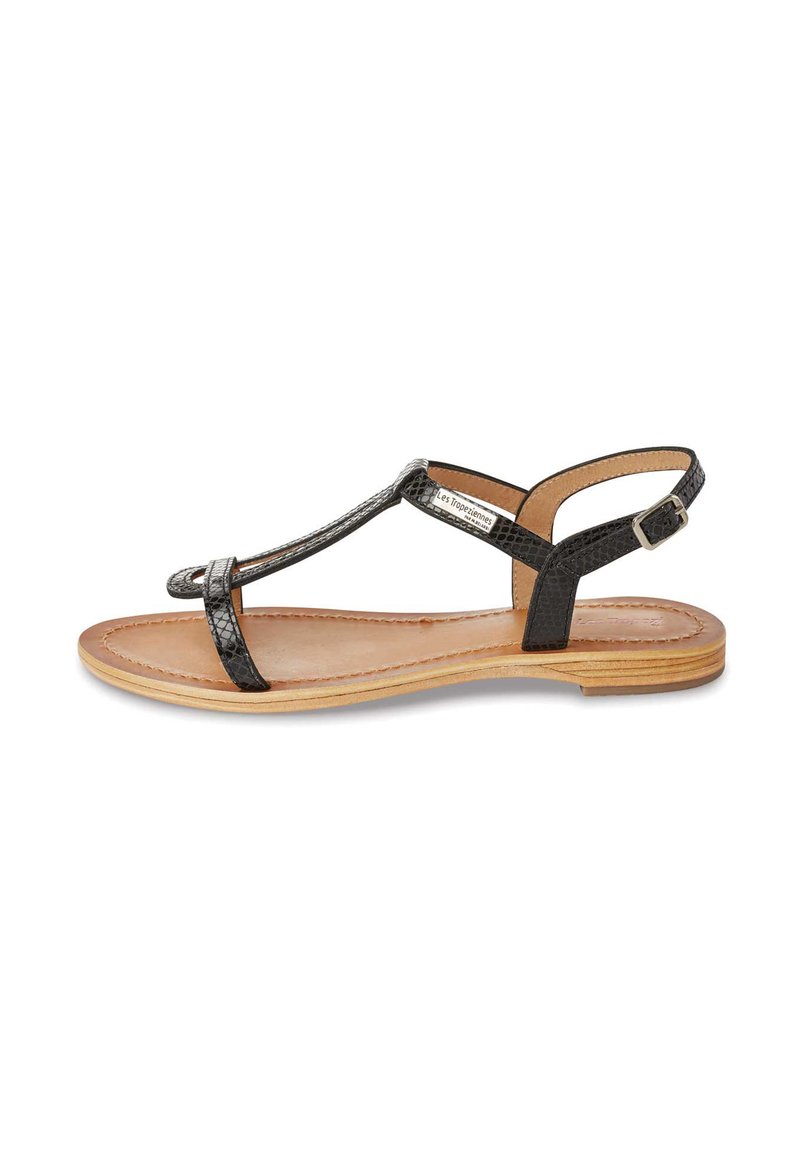 Black, textured leather sandal with T-strap design, flat sole, and adjustable ankle strap. Natural-colored inner lining and light outsole.
