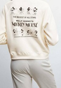 Cremefarvet sweatshirt med et trykt retro Mickey Mouse design på ryggen, der viser illustrationer og tekst i sort. Blød tekstur, afslappet pasform.