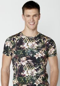 Fekete, rövid ujjú ing fehér orchidea és zöld levelek mintázatával, puha anyagból készült, kerek nyakkivágással.