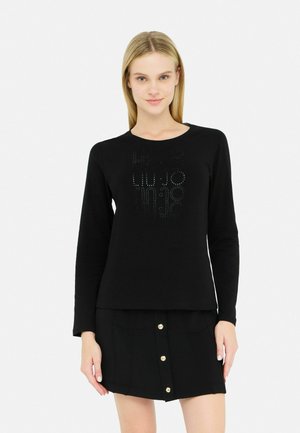 Zwarte langesleeve shirt met een ronde halslijn, voorzien van een textuurontwerp en metalen accenten. Gecombineerd met een zwarte rok met knopen aan de voorkant.