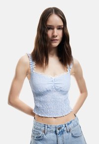 Blå gingham crop top med flæsedetaljer på stropperne og blondekant, prydet med smocked stof og en volangkant. Kombination med denim shorts.