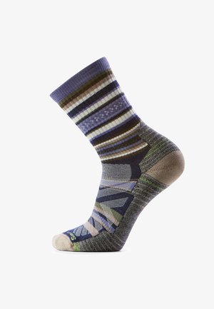 Kolorowa skarpeta do połowy łydki w poziome paski w kolorach fioletowym, brązowym, zielonym i białym oraz z geometrycznymi wzorami na części stopy i pięty.