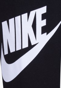 Juodi medvilniniai leggingai su ryškiu baltu Nike logotipu ir swoosh raštu. Lygus paviršius, prigludusi arba figūrą apimanti forma.