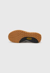 Semelle en caoutchouc avec une surface brune texturée, dotée d'accents noirs et d'un logo jaune. Bords lisses et détails arrondis et décorés visibles.