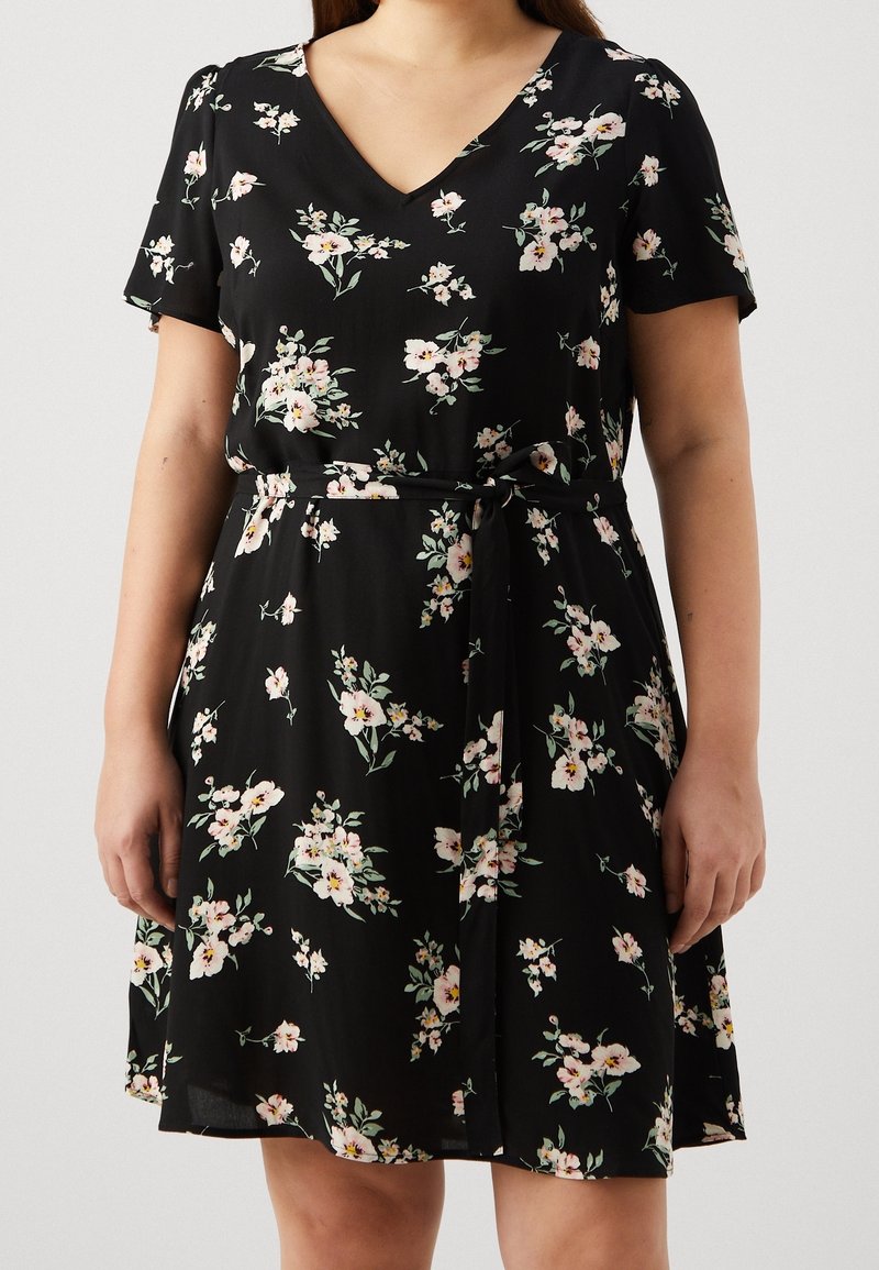 Robe florale noire à manches courtes, décolleté en V, avec une ceinture à nouer à la taille. Présente des motifs de fleurs roses et blanches sur un tissu léger.