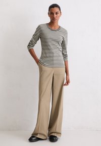 Szara i biała koszula w paski z długim rękawem, zestawiona z beżowymi szerokimi spodniami i czarnymi płaskimi butami, o prostym, okrągłym dekolcie.