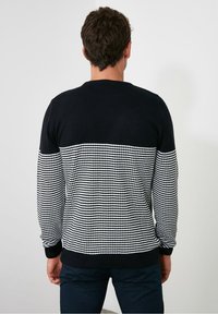Gestrickter Pullover mit einem oberen Bereich in navyblau und einem schwarz-weißen Hahnentrittmuster im unteren Abschnitt. Gerippte Bündchen und Saum.