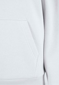 Tissu de sweat-shirt gris clair avec une poche kangourou, bordures côtelées aux poignets et à l'ourlet ; texture lisse et design simple.