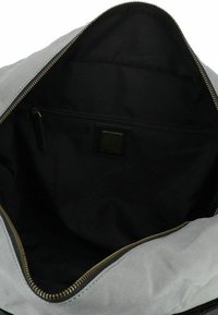 Intérieur de sac en toile de couleur gris clair avec une texture lisse. Présente une doublure noire foncée et une poche zippée avec une petite étiquette logotypée. Fermeture éclair.